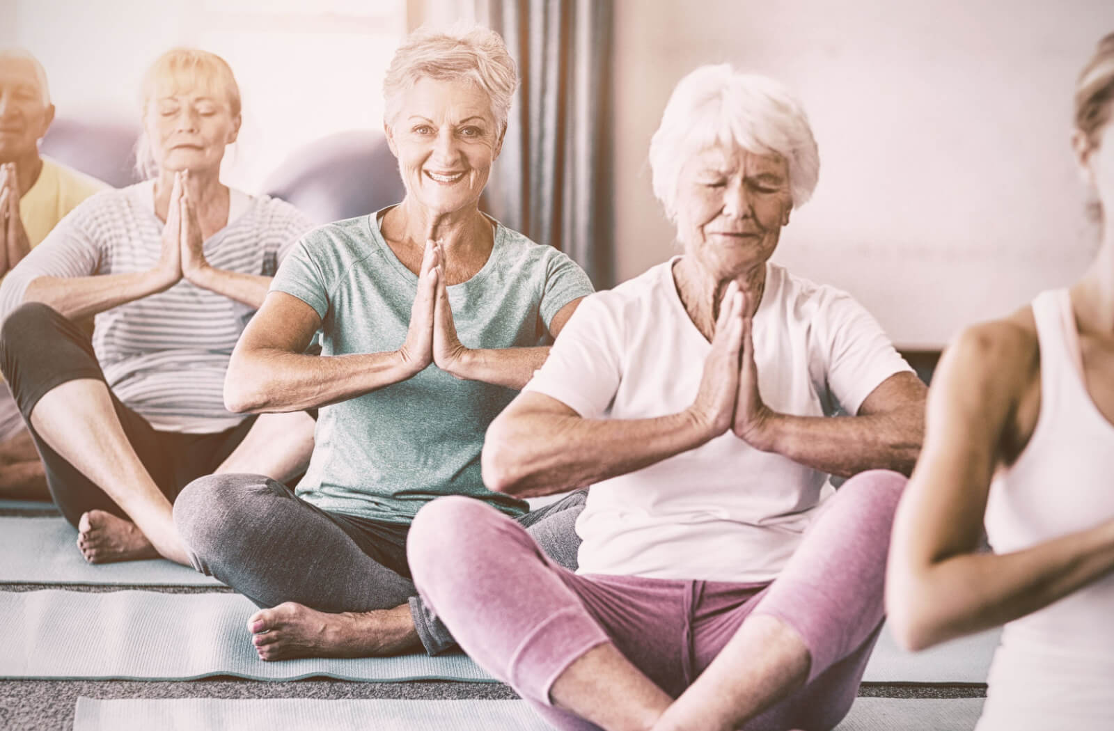 A group of seniors in a yoga class doing a seated prayer pose.