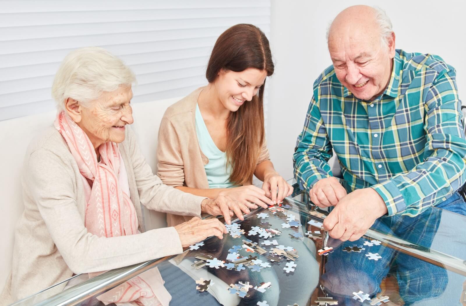 A pair of older adults solving a jigsaw puzzle with the assistance of a memory care staff.