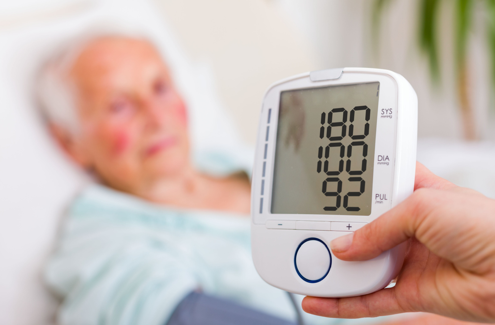 A close up sphygmomanometer screen reveals an alarming high blood pressure reading from a senior with vascular dementia sitting on the couch at home