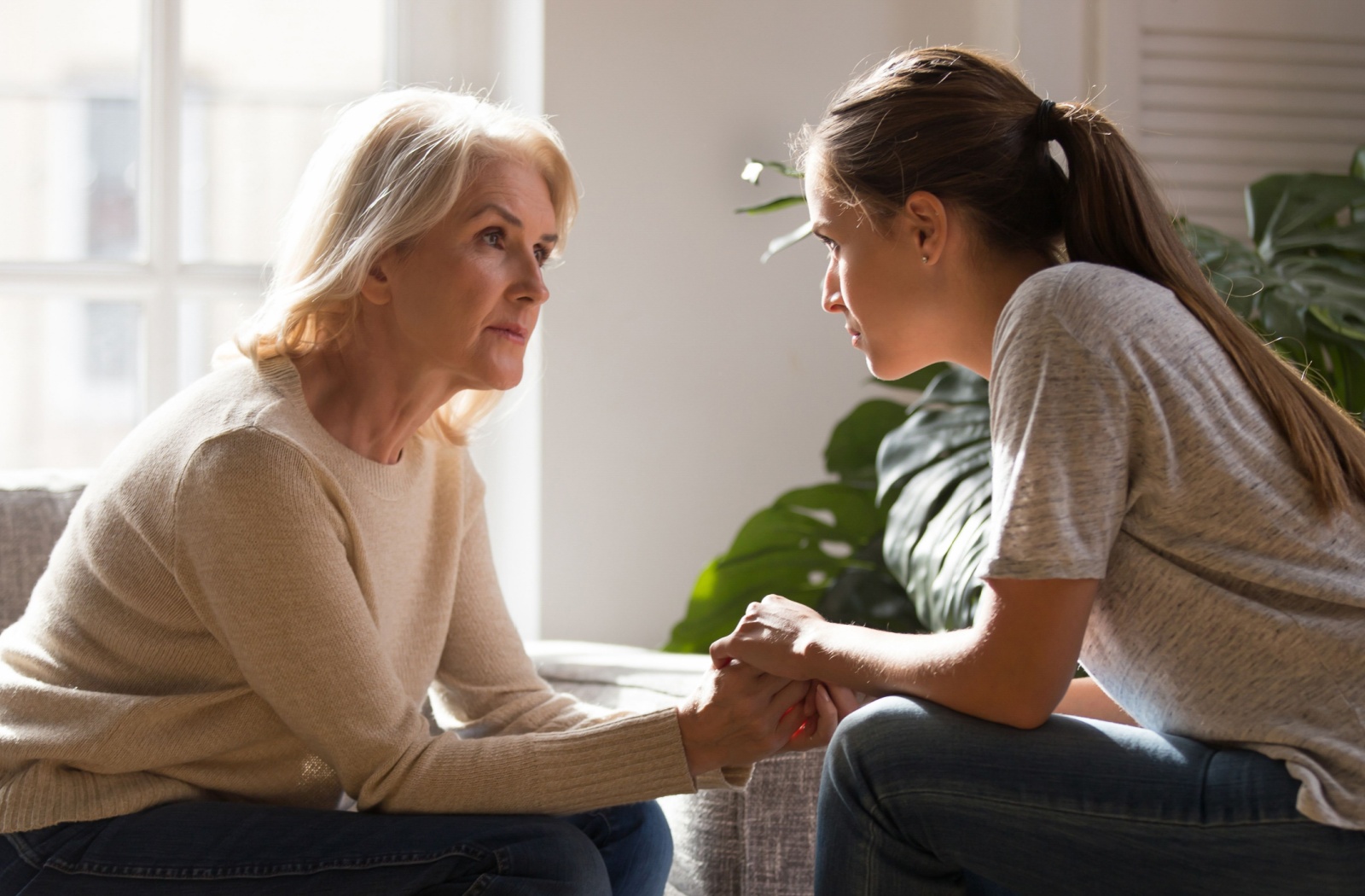 A young adult sitting across from their parent with dementia looking into each others eyes during a conversation.