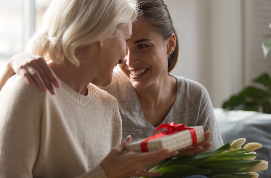 An adult and their parent touching foreheads together in appreciation while holding a gift and white tulips.