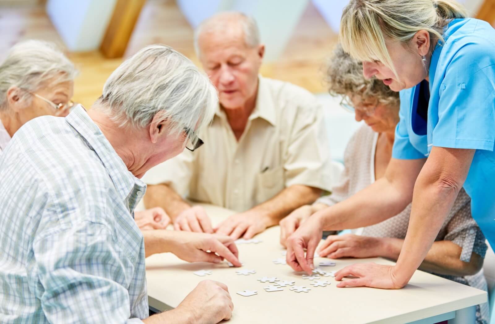 A group of older adults with dementia doing a puzzle with a staff member.