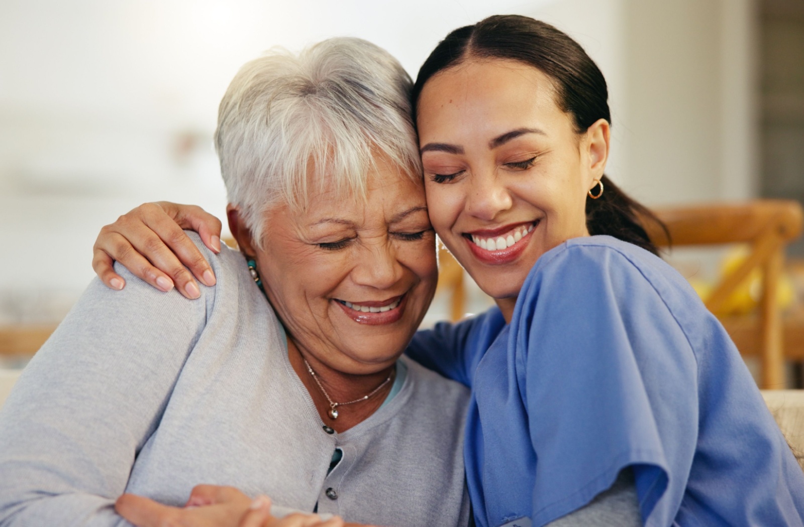 A caregiver and resident in memory care smiling and hugging each other.