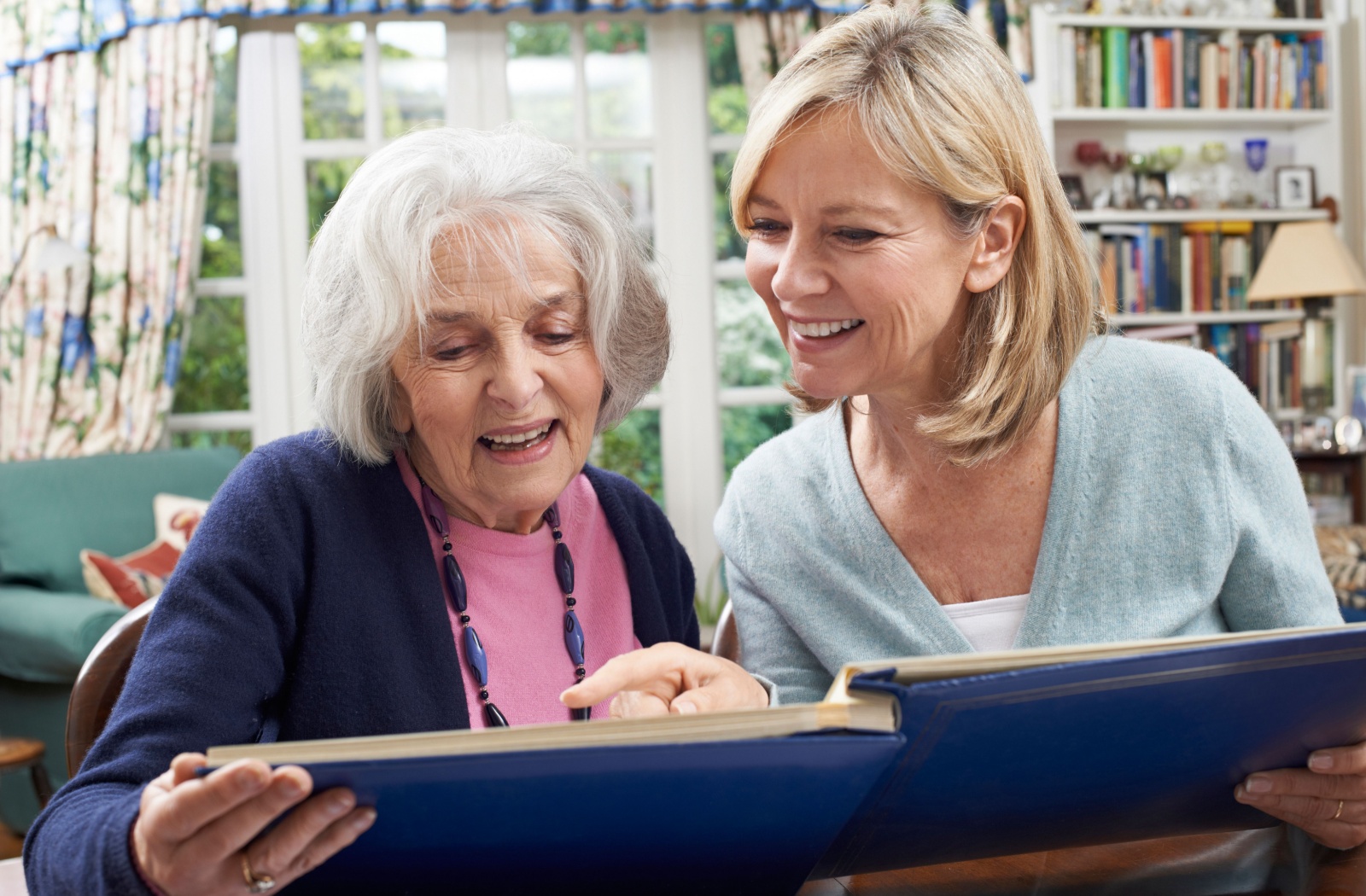 A resident in memory care showing their adult child a photo album while they both smile and reminisce.