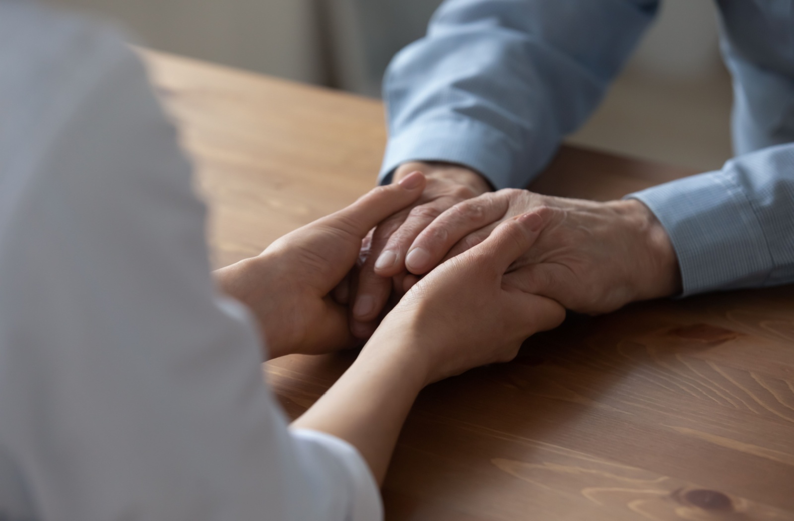 An adult child holding the hands of their older parent to reassure them.