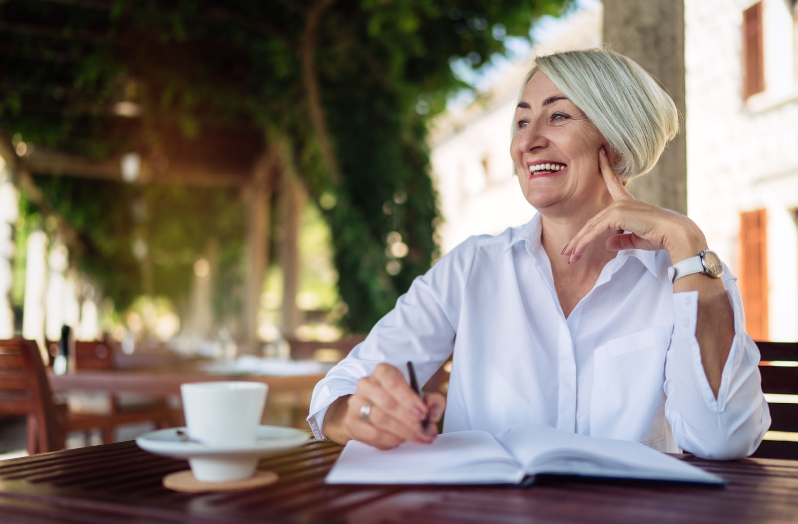 A senior writes in their journal to strengthen their cognitive abilities while having coffee outside