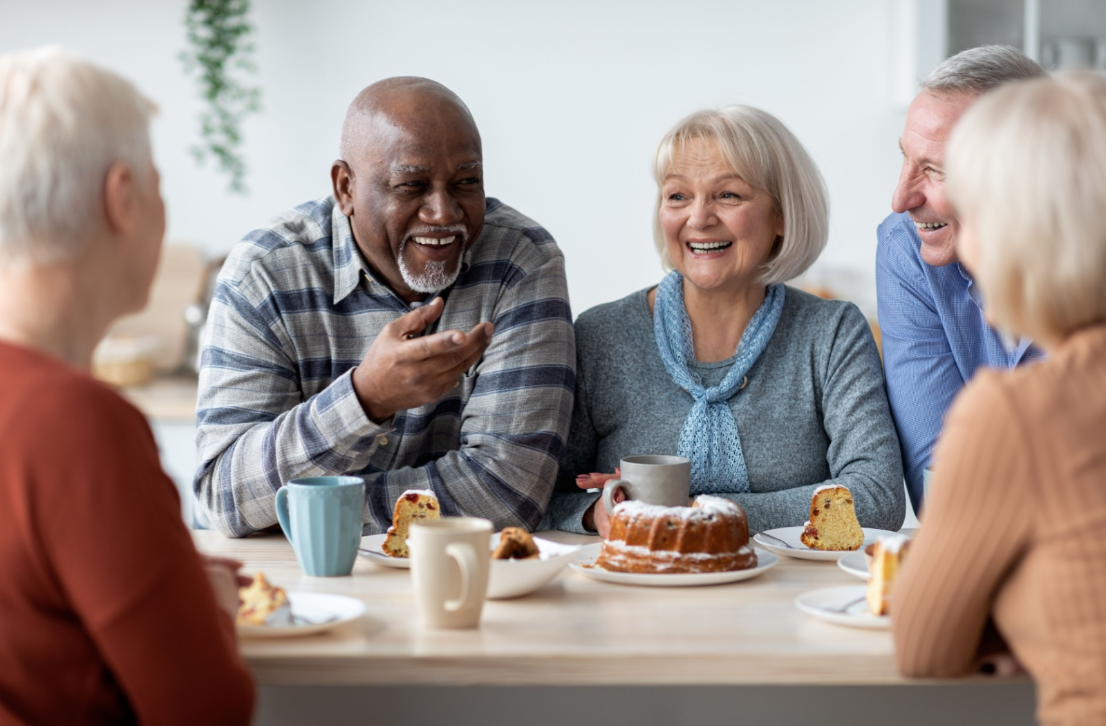 A group of seniors in memory care enjoying tea and snacks while seated at a table together.