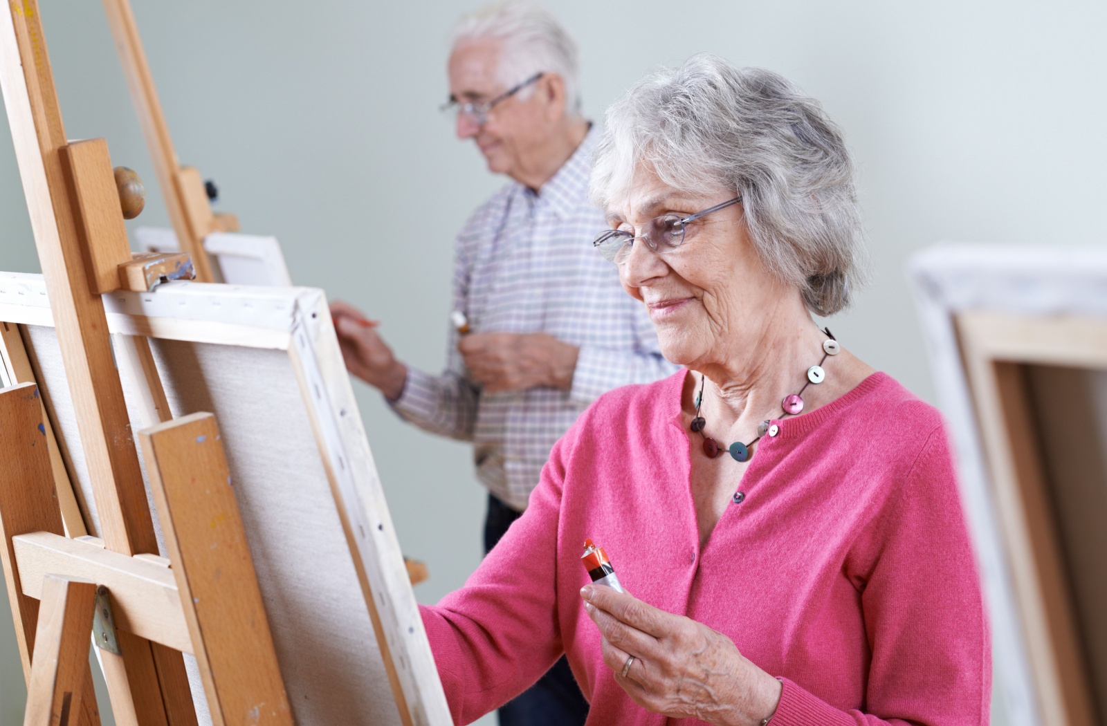 2 older adults in memory care paint on individual canvasses on easels during an art therapy class