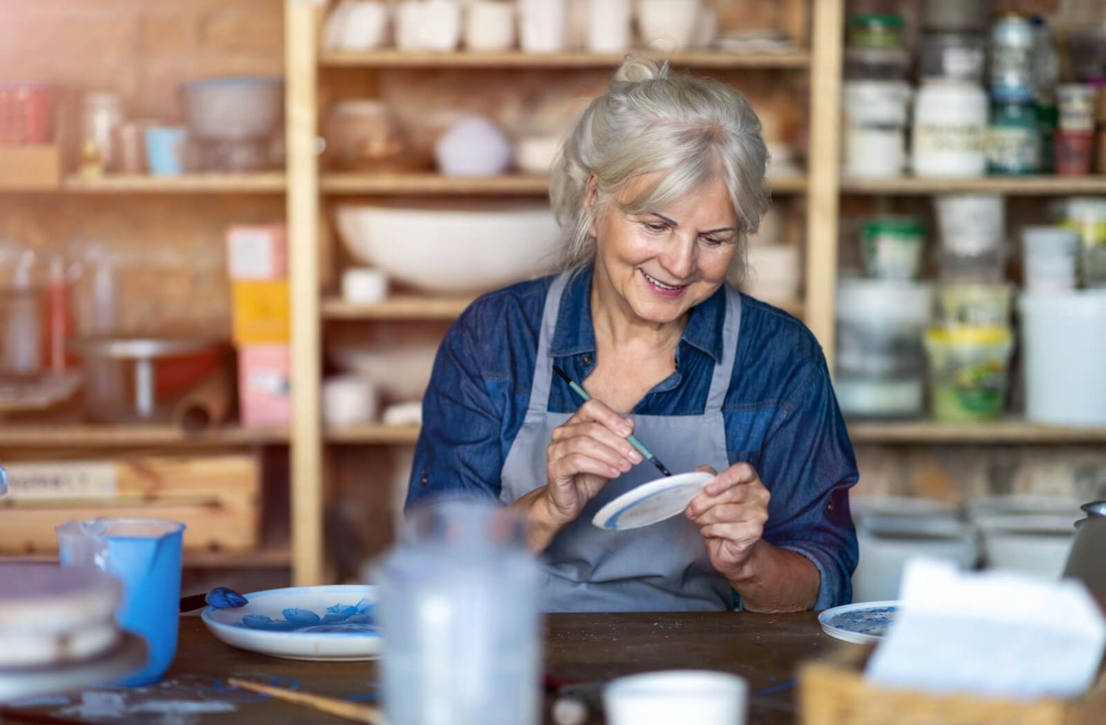 An older adult smiles while painting a piece of pottery in an art shop during a creative class in senior living